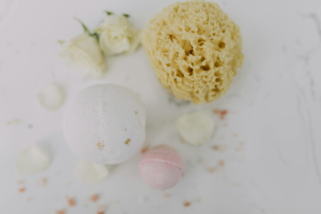 Flat lay of spa essentials featuring bath bombs, sponge, and rose petals for a relaxing experience.