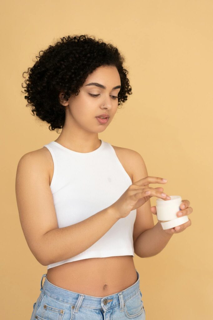 Woman with curly hair applying skincare product in a studio setting.